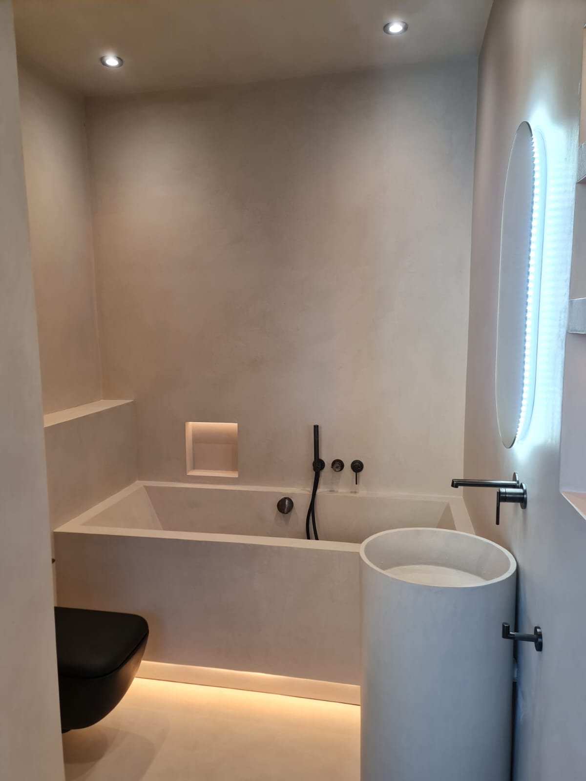 Finished microcement bathroom with bespoke bath, basin and lit niche